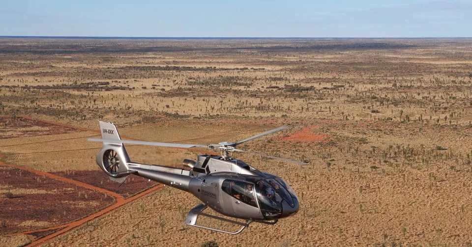 A helicopter flying over red desert ranges